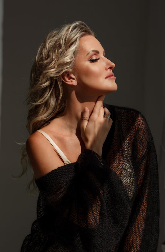 Woman with styled hair and makeup, wearing a dark sweater against a neutral background